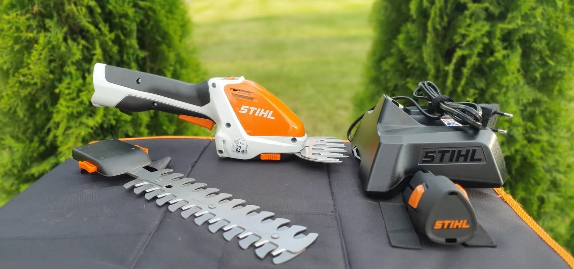 STIHL Akku-Strauchschere mit Ladegerät und Akku auf einem Tisch im Grünen